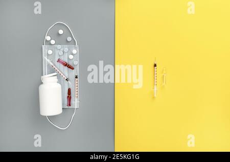 Mock-up bottle with spilled pills, syringes, ampoules and medical mask on trendy yellow and grey background. Medicine background. Coronavirus vaccine Stock Photo