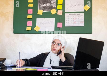 Muslim women working in the office from home using laptop and mobile phone for any support Stock Photo