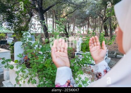 muslim woman rising her hands praying to allah for the dead peoples in a graveyard will Stock Photo