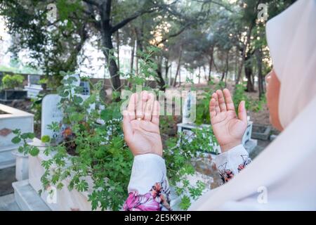 muslim woman rising her hands praying to allah for the dead peoples in a graveyard will Stock Photo