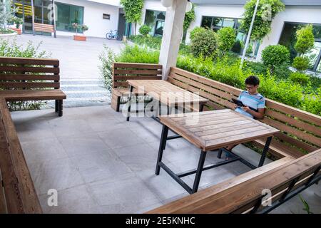 Lonely boy using tablet in the garden sitting on a bench Stock Photo
