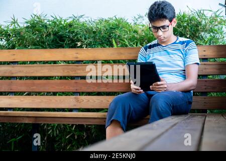 Lonely boy using tablet in the garden sitting on a bench Stock Photo