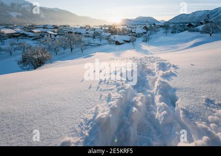 Deep snow track through winter landscape during sunset in alpine village with sun star between mountains, Wildermieming, Tirol, Austria Stock Photo