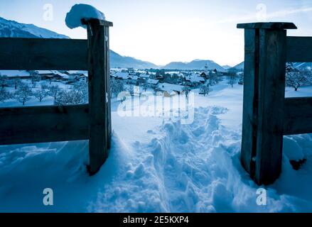 View through fence to alpine winter landscape during blue hour dusk with view over small Austrian traditional village in Wildermieming, Tirol, Austria Stock Photo