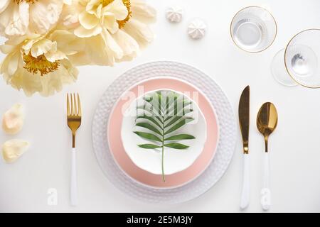 Effortless golden birthday dinner table decor. Pale yellow peony flowers and Late Spring, Summer flat lay. White dinner table, white and gold utensils Stock Photo