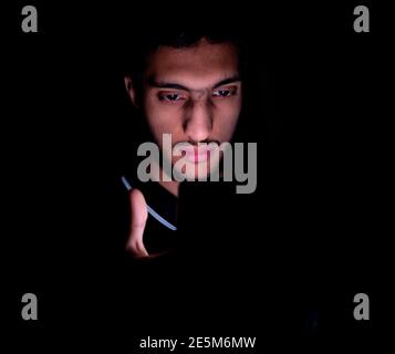 Portrait of middle eastern guy checking his phone in a dark room Stock Photo
