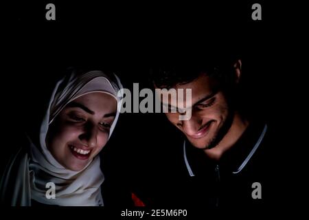 portrait of middle eastern guy and girl using their phone in a dark room Stock Photo