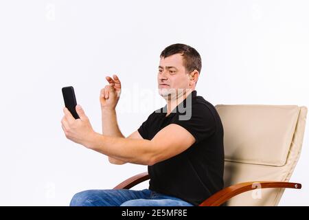 A man sitting in a chair communicates with the help of gestures via video communication, showing a gesture no. White background. Stock Photo