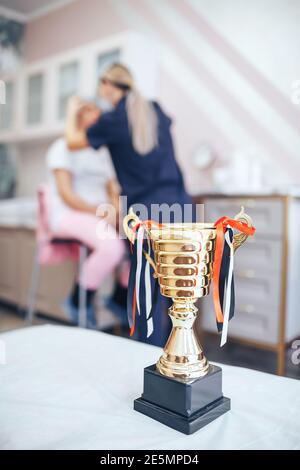 Cosmetolog beauty master making marks with pencil before the permanent makeup procedure with winner cup on the main plan Stock Photo