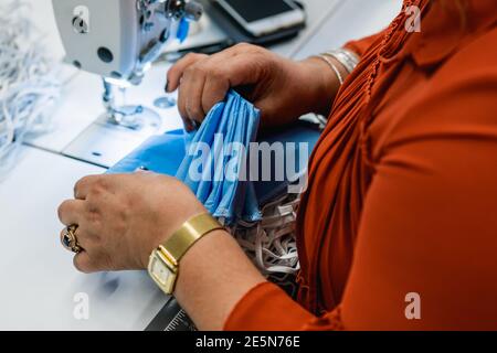 Closeup image of a woman's hands working on a sewing machine in a mask factory Stock Photo
