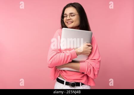 Photo of attractive lady in glasses, sweet holds laptop, wears casual pink t-shirt white pants isolated pink color background Stock Photo