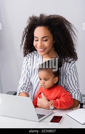 happy african american freelancer sitting with toddler daughter while working from home Stock Photo