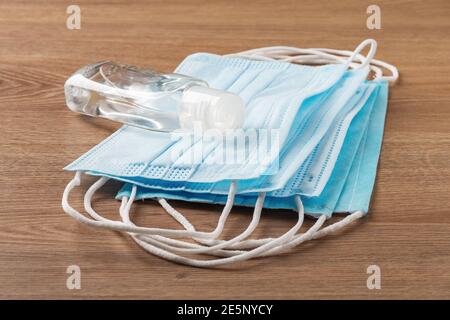 Disinfecting hand sanitizer in a small bottle on a heap of disposable medical face masks on a brown desk. Personal protection against viral infections Stock Photo