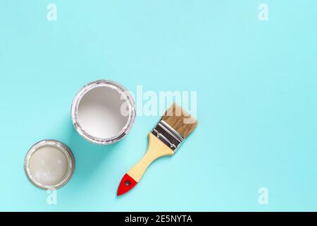 Paint brush with wooden handle and open white paint can on a cyan blue background. Construction painting work, repair and redecorate concepts. Stock Photo