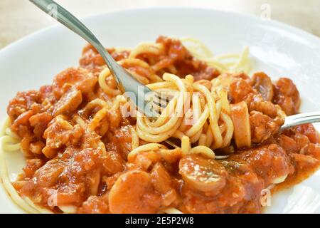 fried spaghetti topping slice sausage with chop pork and ketchup roll over fork on plate Stock Photo
