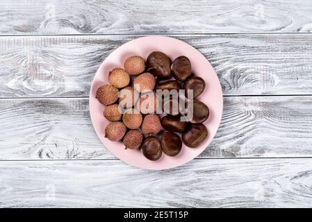 Fresh lychee an chestnuts on the plate on a wooden background. Stock Photo