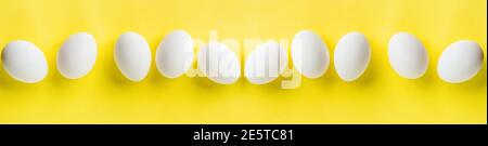 Many white chicken eggs lying in row on a yellow trendy background. Easter minimal creative composition with copy space. Spring Happy Easter holiday G Stock Photo