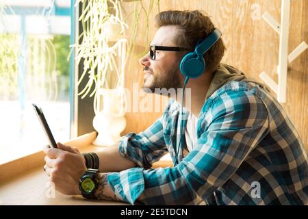 Happy young freelancer man listening to music using tablet computer sitting inside coffee shop Stock Photo