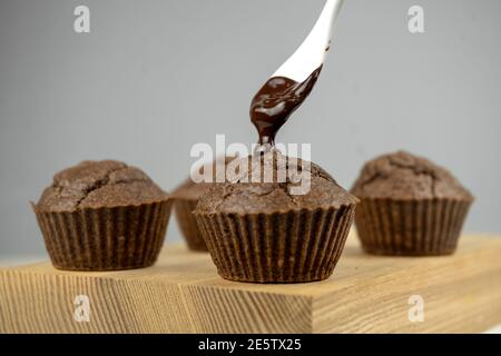 Pouring melted chocolate to chocolate brown muffins on wooden board Stock Photo