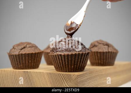 Pouring melted chocolate to chocolate brown muffins on wooden board Stock Photo