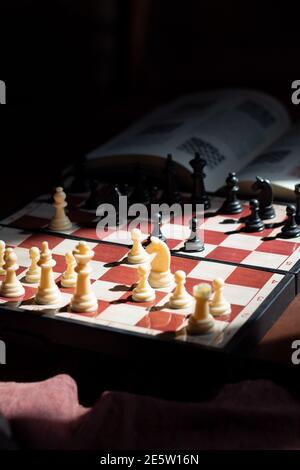 A chessboard showing the spanish opening and an open chess book over a dark background. The image represents deep understanding and study of chess. Stock Photo