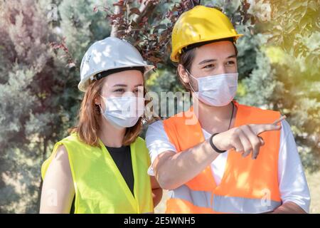 Portrait of worker and engineer wearing face masks checking production process and discussing project details on construction site. New normal. Stock Photo
