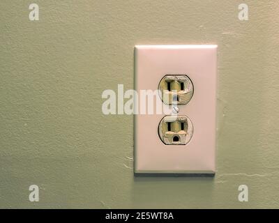 White electrical wall outlet with two sockets mounted on a green painted wall. Stock Photo