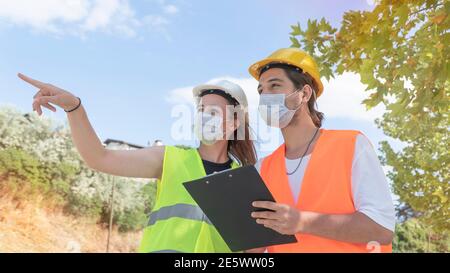 Portrait of worker and engineer wearing face masks checking production process and discussing project details on construction site. New normal. Stock Photo