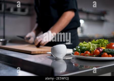 chef cook in medical gloves prepare greek salad or chop vegetables at kitchen  Stock Photo