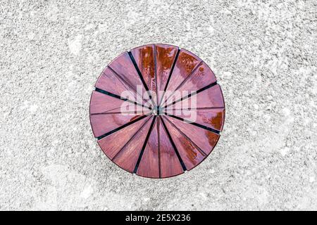 Close-up from above of pie pattern circular handmade vintage tabletop in brown varnished wood with light reflections standing on raw concrete ground Stock Photo