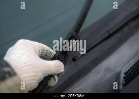 A hand in glove holding a damaged windscreen wiper blade, outdoor closeup Stock Photo