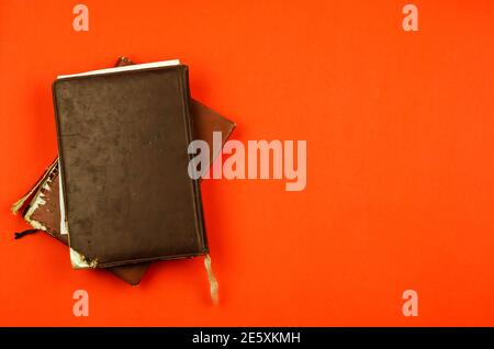 Old Tattered diaries on red background. Two closed Diaries in brown and black tattered cover with no lettering. Flat lay, copy space Stock Photo