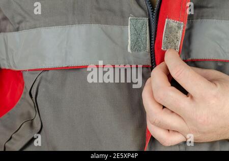 Special protective clothing for work. The man's hand is buttoning a gray work jacket with red inserts. Close-up, selective focus. Stock Photo