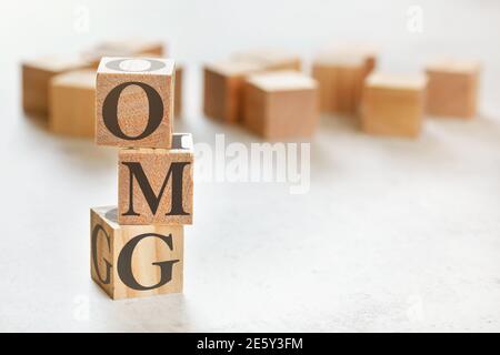 Three wooden cubes with letters OMG (short for Oh my God), on white table, more in background, space for text in right down corner Stock Photo