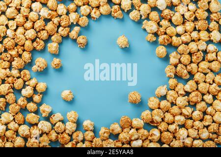 Popcorn is scattered on a blue background, in the form of a frame. Yummy for the filming of movies, TV series, cartoons. Free space, top view Stock Photo