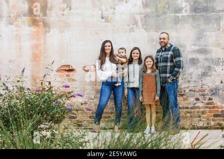 A family of five with two girls and a baby boy standing by an urban old brick wall Stock Photo