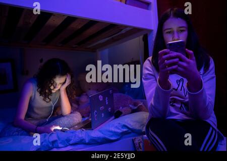 Teenage girls on laptop and phone screens in their bedroom during lockdown Stock Photo