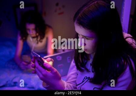 Teenage girls on laptop and phone screens in their bedroom during lockdown Stock Photo