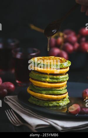 Green and yellow pancakes with matcha tea or spinach, corn flour and turmeric, dressed honey. Dark background. Stock Photo
