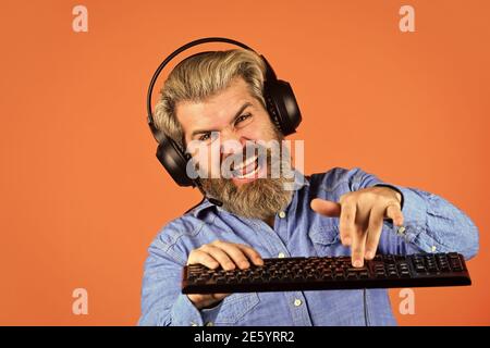 Man bearded hipster gamer headphones and keyboard. Gaming addiction. Superior performance. Online gaming. Modern leisure. Run any modern game. Graphics settings pushed to limit. Play computer games. Stock Photo