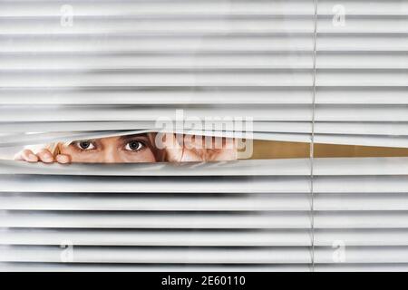 Young woman looking through Venetian blinds Stock Photo