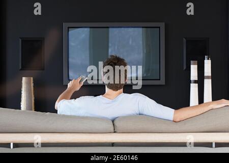 Rear view of young man using remote control while sitting on couch in living room Stock Photo