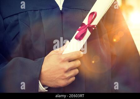 Closeup of young male student holding diploma on graduation day Stock Photo