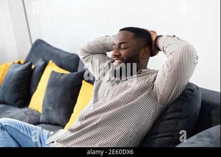 Relaxed young african man resting on comfortable couch holding hands behind head, millennial hipster guy enjoy no stress peace of mind lounge on sofa Stock Photo