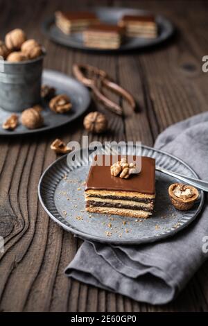 Gerbeaud bars filled with plum marmalade and crushed walnuts, topped with chocolate frosting on wooden background Stock Photo