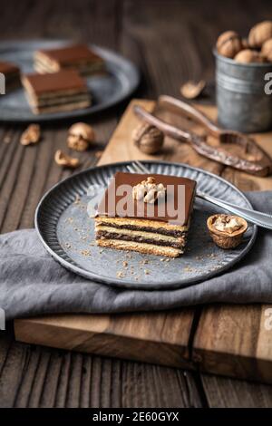 Gerbeaud bars filled with plum marmalade and crushed walnuts, topped with chocolate frosting on wooden background Stock Photo
