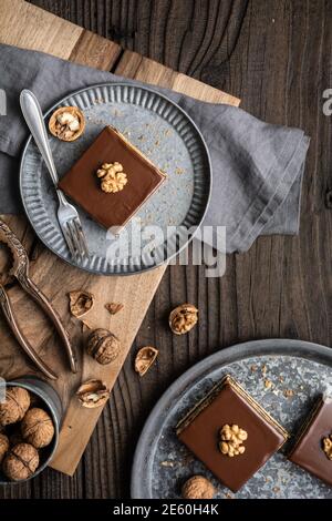 Gerbeaud bars filled with plum marmalade and crushed walnuts, topped with chocolate frosting on wooden background Stock Photo