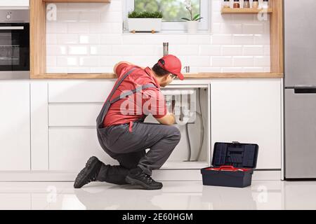 Plumber kneeling and fixing a pipe under sink in a modern kitchen Stock Photo