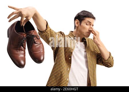 Man blocking his nose and holding a pair of smelly shoes isolated on white background Stock Photo