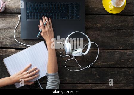 Top view of a woman working or studying from home using laptop computer and writing in notepad. Stock Photo